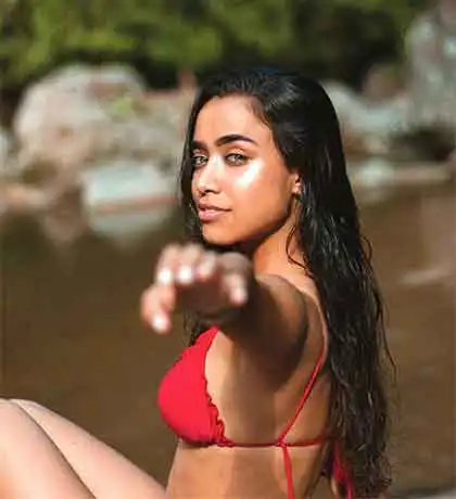 A photo of a beautiful Latina woman in a red bathing suit extending her left arm out to the photographer